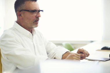 Kırpılmış görüntü şık optik gözlükler ve masaüstü ofis İçişleri oturan giymiş beyaz gömlek olgun iş adamı. Kopyalama alanı alanı reklam metin iletinizi için