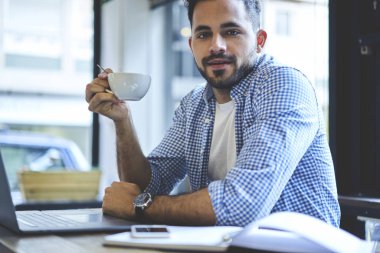 Portre yakışıklı sakallı Freelancer holding çay dinlenme Kupası zevk ara kafe iç dizüstü bilgisayar, dosya karşıdan yüklerken kahve molası zevk profesyonel metin yazarı kullanan çalışırken