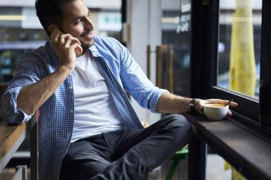 Serbest zaman ve arkadaşça mobil sohbet, zevk kafeteryada oturan genç yakışıklı Yöneticisi kayıtsızca giyinmiş kahve molası planları eğlence için tartışmaya sırasında telefonda konuşurken erkek öğrenci