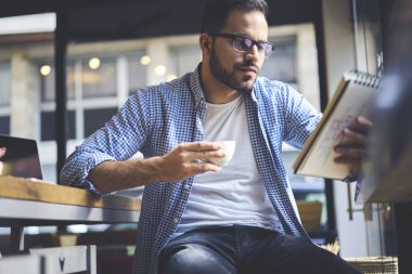 Yakışıklı sakallı grafik tasarımcı taslak strateji geliştirme sırasında kahve molası, yetenekli öğrenci bilgi analiz kurs notları kontrol hakkında not defteri düşüncesinde yazım denetleme