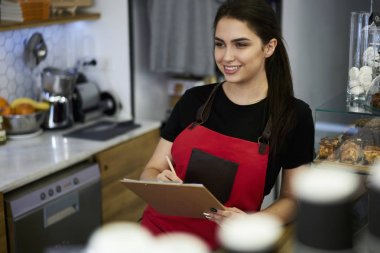 Uzağa bakarak ve sipariş yapmak için denetim listesi kayıtlarının yazarken gülümseyen çekici barista. İşyerinde ayakta ve kendi restoran iş geliştirmek için bilgi belirterek neşeli garson