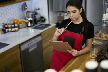 Düşünceli kadın sahibi kafe düşünce geliştirmek için fikirleri ve kar iş duran ahşap bar. Profesyonel barista Tekdüzen lezzetli kahve yeni türleri oluşturma üzerinde durulması içinde giyinmiş 