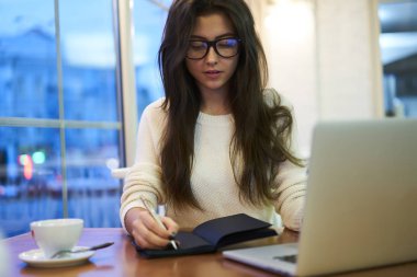 Çalışma görev çalışma alanı dizüstü bilgisayar, Not Defteri'nde yazma accountings için ağlar ve uygulamasını kullanarak yaratıcı tasarımcı ile oturan planlar gözlük profesyonel kadın Yöneticisi