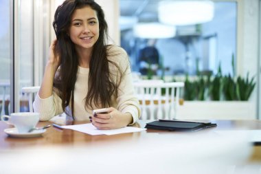 Smartphone, kahve molası bulanık kopyalama alanı alanı reklam için oturan esmer kadın manifatura iletileri e-posta kutusunu kontrol etmek için kafede Wi-Fi erişimi kullanarak genç neşeli öğrenci portresi