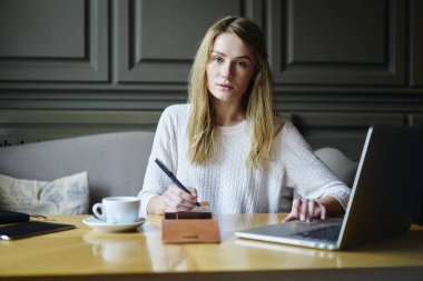 Yarım uzunluk portre kadın Freelancer bilgi ders kitabı kayıt ve dizüstü bilgisayarda tarama sırasında kameraya bakıyor. Muhteşem kadın rahat kafede modern cihaz ile çalışma