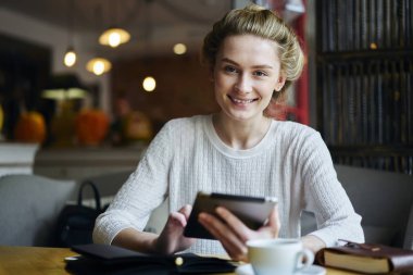 Dokunmatik holding neşeli hippi kız portresi pad el oturma alanı coworking. Gülümseyen ve kamera dijital tablet için 4 g bağlayan ağ süre bakarak olumlu öğrenci internet