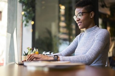 Genç siyah modeli zamana Cafe iç harcama sosyal ağlar sohbet gülümseyen, afro Amerikan erkek web tasarımcısı projede çalışan dizüstü bilgisayardaki uygulama kullanılarak gözlük içinde 