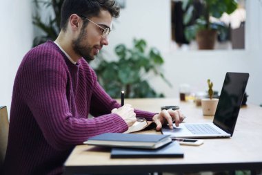 Modern bilgisayar eğitim webinar izliyor ve metin bilgileri Not Defteri'nde belirterek optik gözlük düşünceli akıllı öğrenci. Erkek laptop çalışma ve notları ders kitabı içinde yapım konsantre