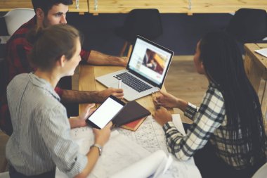 Genç tasarımcılar ahşap masaüstü planları ve modern macbook bilgisayar ile oturup yeni grafik oluşturma tartışıyor. Dokunmatik yüzey iş için kullanarak çeşitlilik grubu. Boş ekran alanı. Reklam alanı