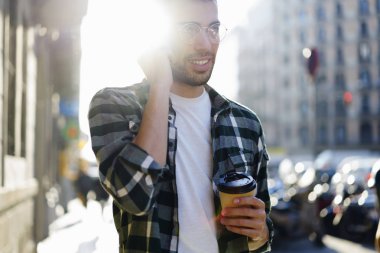 Genç dikkatle güneşli şehirde gezinme sırasında dinleme arkadaş grubu mobil konuşmayı hipster adam sakallı. İyi görünümlü turist gezici servis kullanma smartphone iletişim