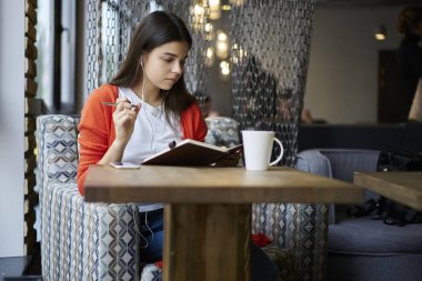 Sevimli kız öğrenci Playlist kulaklık ile modern akıllı telefon dinleme gözde şarkı süre Not Defteri'nde yazılı notlar okuma. Çekici hippi kız elinde müzik keyfi defter ile