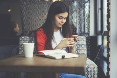 Kulaklıklar ile en sevdiğiniz şarkıları dinleme ve ders kitabı ile yer coworking otururken telefonla sms mesaj gönderme çekici öğrenci. Serbest zaman sırasında cep üzerinde güzel kadın manifatura