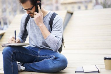 Kentsel ayarlarında oturan günlüğüne notlar yaparken Smartphone'da alarak gözlük öğrencinin resim kırpılmış. Telefon görüşmesi sırasında Not Defteri'nde kroki çizim sırt çantası ile sakallı gezgin