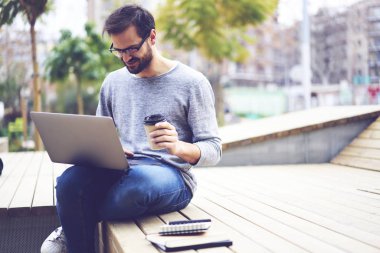 Optik gözlükler lezzetli kahve ve rekreasyon zaman kentsel ayarlarında tadını çıkarırken sosyal ağlar komik video izlemek gülümseyen hipster adam. Kopyalama alanı alanı reklam metin iletinizi için