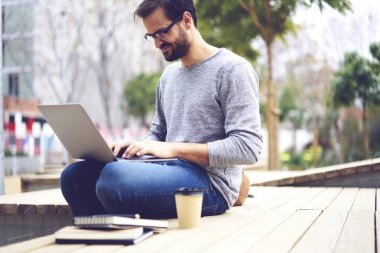 Açık havada oturma modern dizüstü bilgisayar üzerinde arkadaşlarınızla sohbet online gözlük neşeli genç yakışıklı adam. Kentsel ayarlarında bilgisayarda internet bilgi arama gözlükler neşeli öğrenci