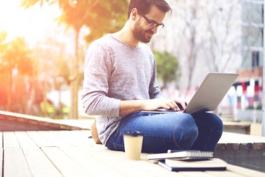 Açık havada oturma modern dizüstü bilgisayar üzerinde arkadaşlarınızla sohbet online gözlük neşeli genç yakışıklı adam. Kentsel ayarlarında bilgisayarda internet bilgi arama gözlükler neşeli öğrenci