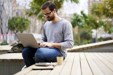 Kampüs içi kahve oturuyor ve kısa mesaj modern dizüstü bilgisayar hızlı 4 g internet bağlantısı kullanarak klavyede yazarak optik gözlük olumlu sakallı hippi adam 