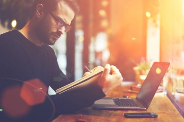 Kırpılmış görüntü dijital bilgisayar başında oturan not defterinde grafik çizim moda gözlük düşünceli erkek tasarımcısının. Genç adam optik gözlükler iş sürecinin planlama yazmaya konsantre