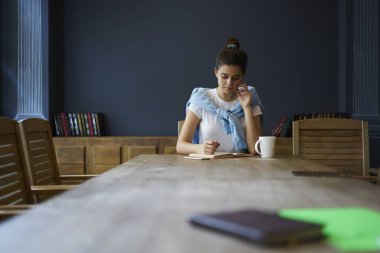 Dalgın zeki öğrenci Kitaplığı'nda oturmuş ödevlerini yaparken şık giyim giymiş. Düşünme hikaye yazma zeki genç bir kadın. Reklam metin mesajınız için promosyon arka plan