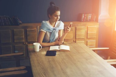 Sosyal ağlar üzerinde dinlenme süre içinde Kütüphanesi'nde ilginç bir kitap ile ahşap masa içinde otururken ücretsiz yüksek hızlı internet bağlantısı kullanarak cep sohbet neşeli yetenekli öğrenci