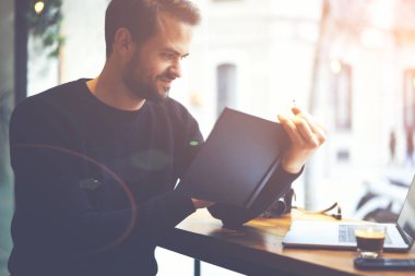 Laptop ile oturma ve defterde yazılı mali belgeler rapor kontrol kahvehane yakışıklı sakallı sahibi. Serbest zaman sırasında ilginç bir komplo yeni kitap okurken erkek öğrenci gülümseyen