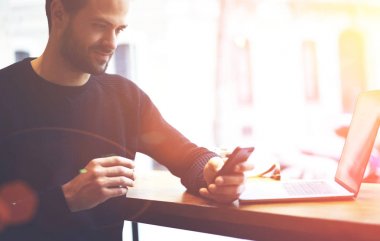 Gülümseyen hipster adam uzaktan kafede dizüstü bilgisayarda çalışırken arkadaş cep telefonu komik sms mesajý okuma siyah kazak giymiş. Kısa mesaj reklam için yer alan kopyalama