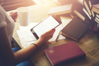 Kırpılmış görüntü Kitaplığı'nda tahta masada oturan kurs proje için bilgi ararken fincan kahve ve promosyon içeriğiniz için boş ekran ile dokunmatik yüzey tutan eller