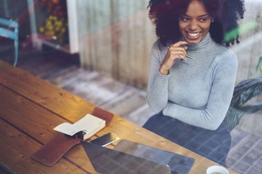 Duygusal gülümseyen afro Amerikan kadın freelancer dizüstü bilgisayarda çalışan için 4 g bağlıyken şık giyim uzağa bakarak giyinmiş. Gülümseyen durulması işkadını kafeterya masada oturan