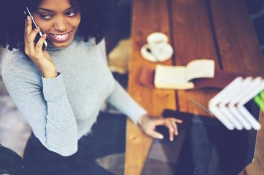 Güzel pozitif afro Amerikan blogger uzaklıkta modern aygıt yolu ile iletişim kurulurken seyir kablosuz internet'e bağlı. Eğlence kafede oturan sırasında cep telefonu üzerinde konuşurken hippi kız