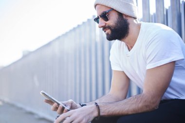 Yakışıklı erkek hipster smartphone ve bloglama için reklam kopya alanı gezici oturuşta 4 g bağlantı kullanarak multimedya dosyaları paylaşımı sosyal ağlar üzerinden güneş gözlüğü manifatura iletilerindeki