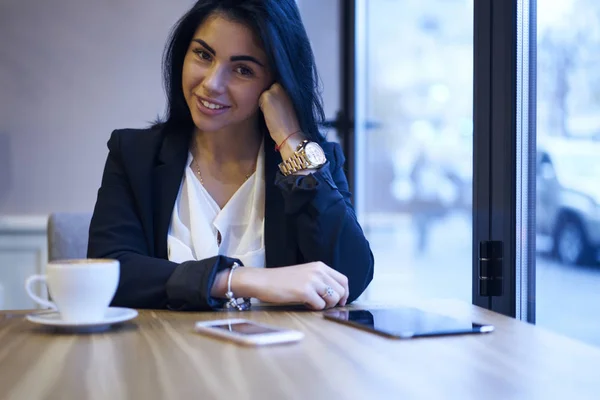 Attractive female administrative manager in stylish weak satisfied with occupation sitting in cozy cafe,portrait of smiling prosperous businesswoman looking at camera resting during coffee break