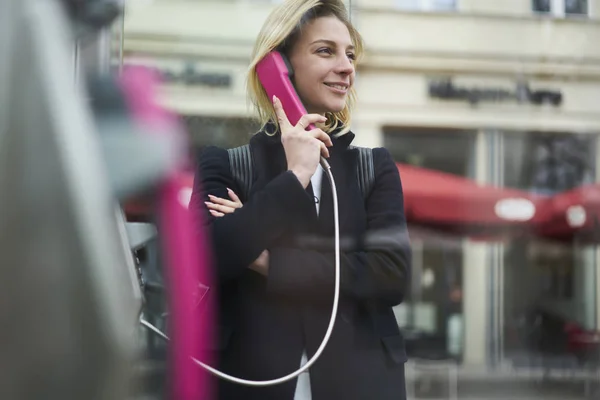 トレンディな服の都市設定の背景の上に立って 旅行者満足を浮かべて週末旅を持つ国際通話接続が良好の公衆電話で話している女性の観光 — ストック写真