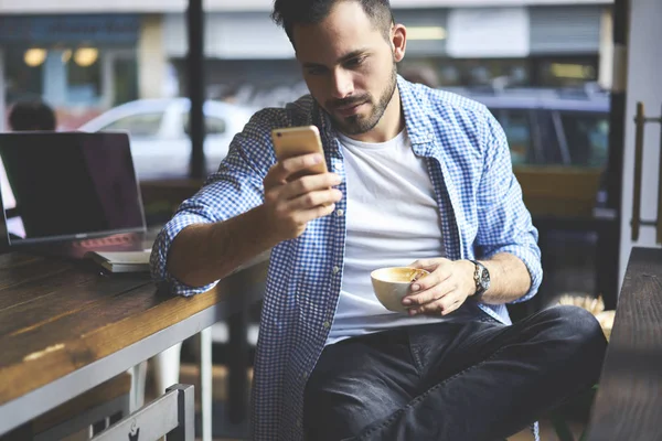集中随意打扮的男性自由职业者检查电子邮件框等待交易使用在线银行服务 严重的时髦家伙安装在智能手机上的咖啡休息时的应用 — 图库照片