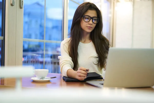 沉思的年轻的黑发雇员在网络观看视频分析信息 专业项目经理在笔记本电脑上工作的眼镜在咖啡馆喝咖啡休息 — 图库照片