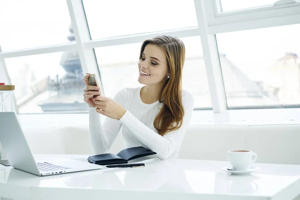 正女性与金发阅读有趣的在线聊天 在现代电话在笔记本电脑上学习 微笑的时髦女孩手机通过高速4G 互联网连接短信 — 图库照片