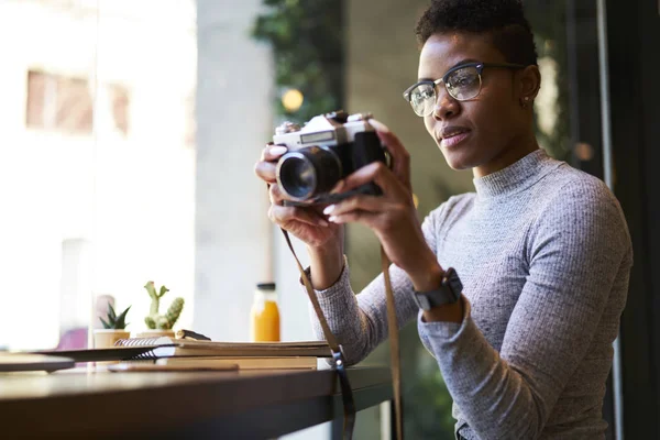 カフェ インテリアの収益金は 創造的なアイデアを使用しての写真をさりげなく若いこと魅力的なアフロ アメリカの写真家ビンテージ カメラで写真を撮る趣味に時間を保留女性ブラック モデルを服を着てください — ストック写真