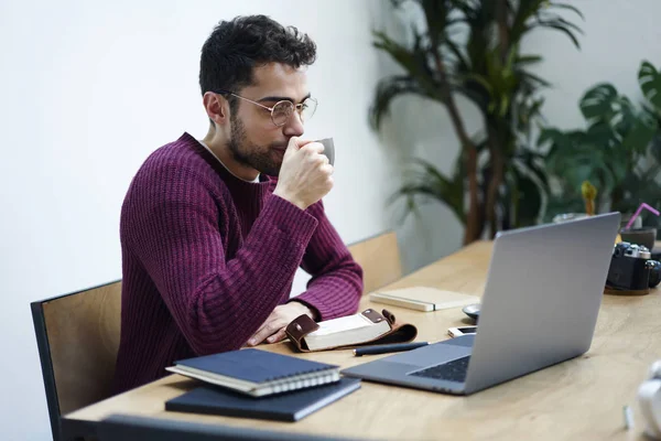 Coworking 空间观看现代笔记本电脑的网络研讨会时 在眼镜欣赏热饮料的创意记者 集中学生在电脑上阅读新闻时喝咖啡 — 图库照片