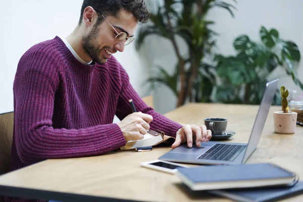 Gülümseyen dizüstü Web sitelerinde bilgi arama ve genel fikirler Kayıt Defteri'nde gözlük girişimci sakallı. Pozitif genç serbest meslek sahibi uzaktan kapalı modern aygıtıyla çalışma