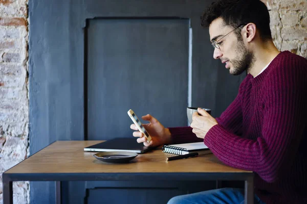 年轻英俊的时髦的家伙穿着休闲服装聊天与朋友在社交网络中使用智能手机连接到无线互联网在办公室里坐在咖啡休息期间 — 图库照片