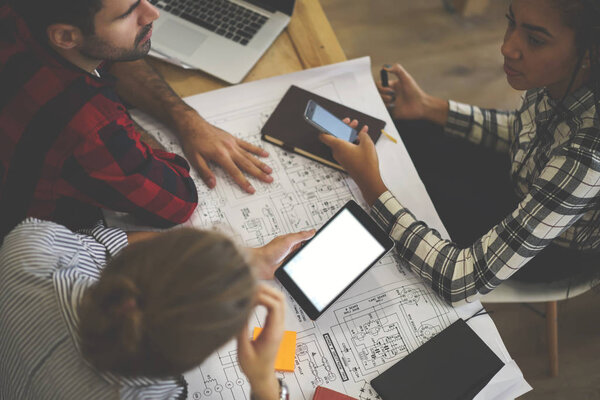 Cropped top view of creative young architects working together on building project using digital tablet and modern telephone for searching information.Blank screen area for advertising content