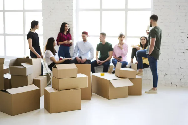 Young people standing in new modern office with stack of boxes near. Team of trendy hipster talking with each ocher after moving to the new office interior. Mock up copy space for your brand name