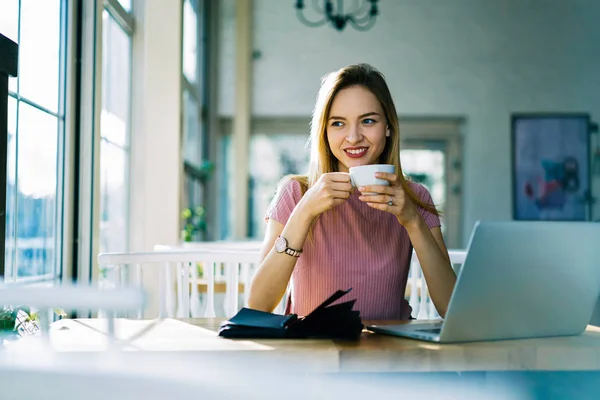 积极的金发项目经理开始工作天与杯茶做远程工作在咖啡馆内部 迷人的记者享受咖啡休息等待反馈坐在笔记本电脑附近 — 图库照片