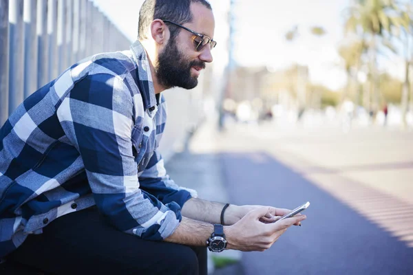 Uśmiechający Się Brodaty Facet Hipster Modnych Okularów Siedzi Zewnątrz Oglądania — Zdjęcie stockowe