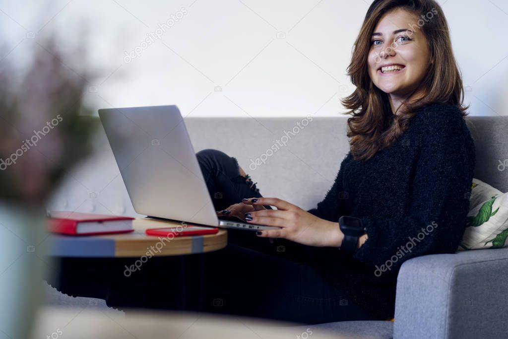 Successful and cheerful skilled freelancer looking at camera while messaging with chief about work on modern device.Smiling charming woman distantly working using application on laptop 