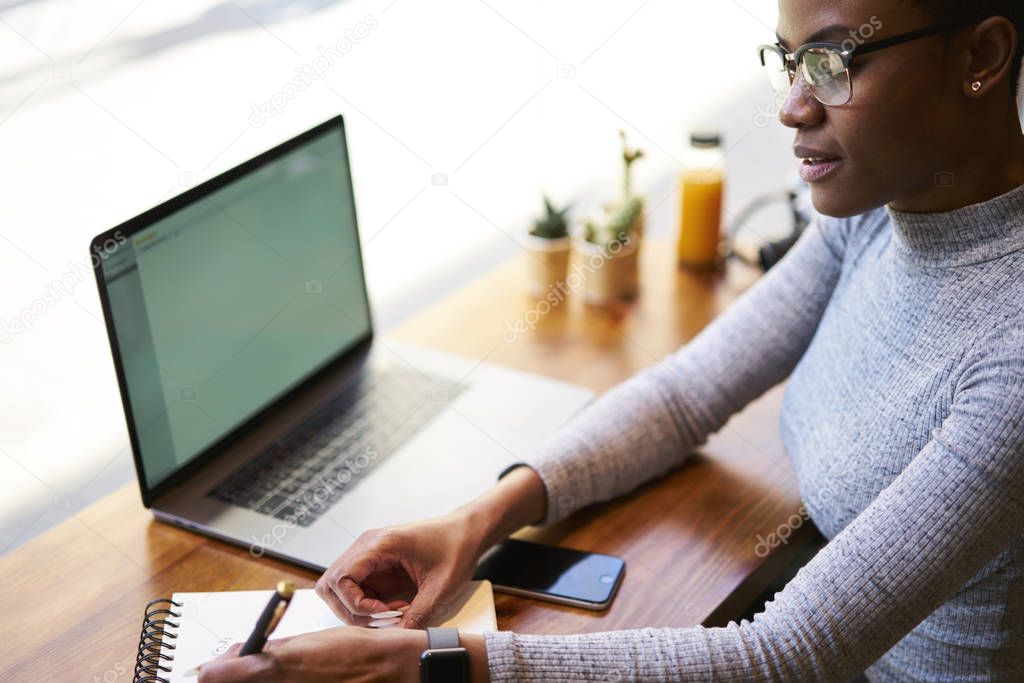 Concentrated afro american copywriter analyzing information making planning of advertising campaign using laptop computer with mock up screen earning money online working with free schedule in cafe