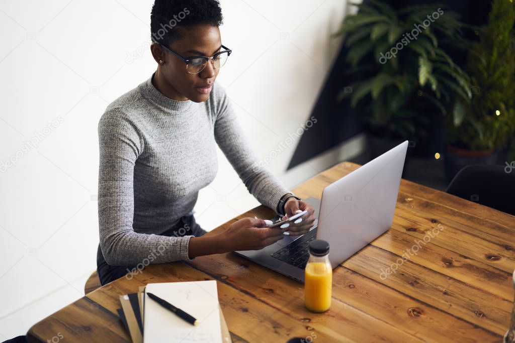 Pensive afro american female entrepreneur checking email box waiting for feedback with online documentation, prosperous business woman dialing number on smartphone while working in cafe interior