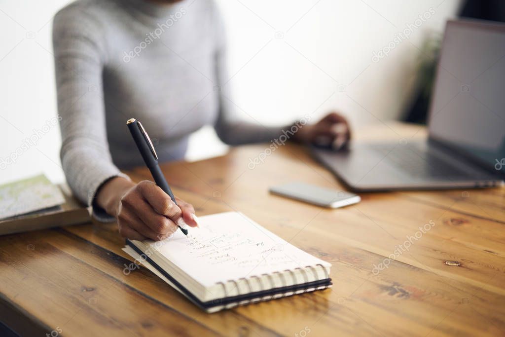 Selective focus on handwriting in notepad with blank pages during creative working process, cropped image of blurred afro american businesswoman copying information from web site using laptop 