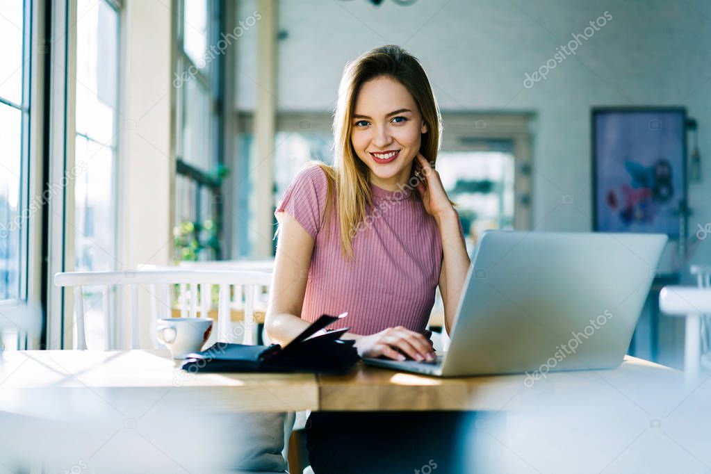 Portrait of smiling blonde author working on freelance enjoying cup of coffee making remote job in cafe interior, charming business manager making financial planning using laptop computer and wifi