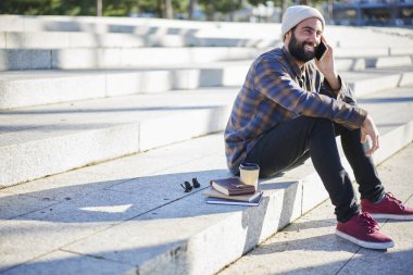 Hafta sonu ve bahar hava kentsel ayarı arka plan, gezici iyi bağlantısı kullanarak neşeli erkek turist üzerinde oturan zevk arkadaş grubu dostu telefonda konuşurken gülümseyen sakallı adam 