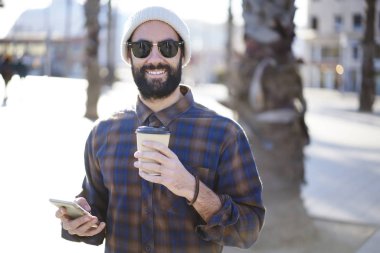 Yarım uzunluk portre gitmek, Erkek turist Smartphone cep telefonu ile yer bulma uygulaması aracılığıyla gezinme neşeli sakallı bir adam açık havada kahve ile gezinme güneşli havanın tadını trendy güneş gözlüğü